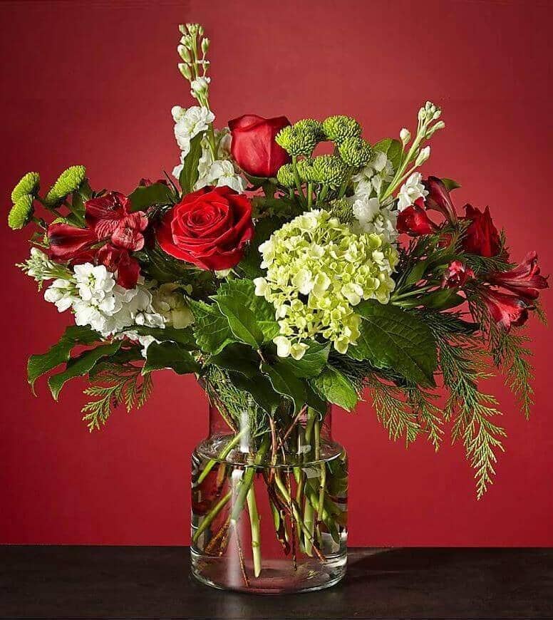 Winter Bright™ Bouquet by Flower Co. is an exclusive handmade arrangement with farm-fresh flowers such as premium hydrangeas, red roses, bright alstroemeria, delicate stock and green button, surrounded by lush foliage.